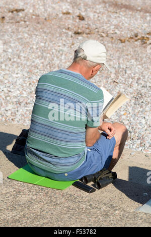 Mann liest ein Buch über die Treppen am Oddicombe Strand an warmen September Tag in Torquay, Devon, England Stockfoto