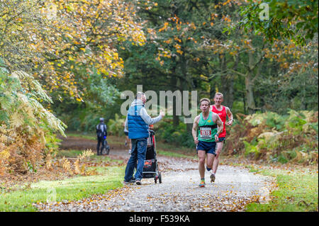 Mann gibt den Daumen nach oben für Läufer läuft in einen Halbmarathon durch einen bewaldeten Park. Stockfoto