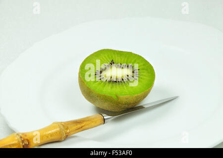 halbierte Kiwis auf weißen Teller mit Messer, Nahaufnahme, Makro, horizontal, weißer Hintergrund Stockfoto