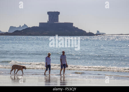 Paar walking Hund am Meer am Strand von St-Ouen Jersey mit La Rocco Tower im Hintergrund Stockfoto