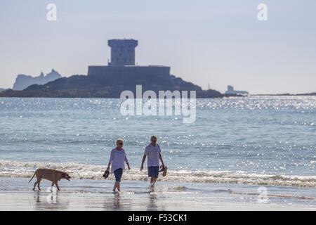 Paar walking Hund am Meer am Strand von St-Ouen Jersey mit La Rocco Tower im Hintergrund Stockfoto