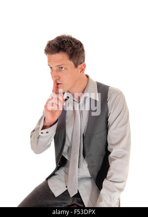 Ein junger Mann in einem grauen Hemd und Weste für weißen Hintergrund mit dem Finger über den Mund sitzt. Stockfoto