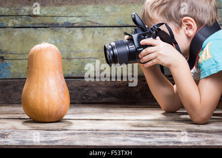 Lustige fair junge verwenden DSLR-Kamera versuchen, Reifen Kürbis auf hölzernen Hintergrund im Studio fotografieren. Fotografie-Unterricht oder lernen Stockfoto