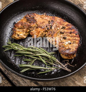 Schließen Sie herauf Bild von gerösteten Beefsteak mit Haufen von Rosmarin auf Grillpfanne. Fleisch-Menü und Rezept-Hintergrund Stockfoto