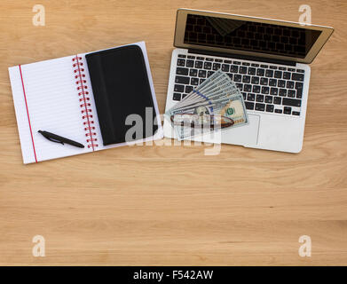 Betriebswirtschaftlicher Hintergrund, Blick von oben auf einem Holztisch - ein Laptop, Notebook und Stift, Visitenkartenhalter und Dollarnoten. Stockfoto