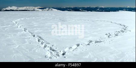 Menschlichen Fußabdruck bilden die Herzform auf schneebedeckten Berg-Plateau und Bergketten hinter. Stockfoto