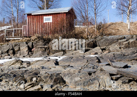 Rote Häuschen am Ufer mit einer Menge von Steinen in den Vordergrund, Foto aus Nordschweden. Stockfoto