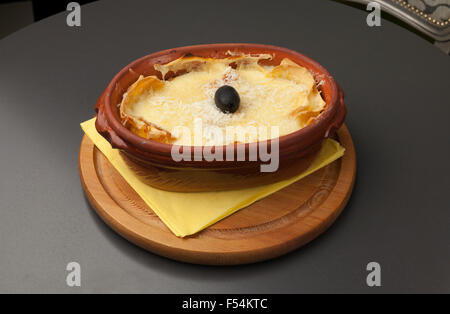 Portion Lasagne in einem Keramiktopf auf einem Holzsockel Stockfoto