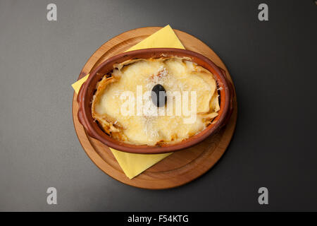 Portion Lasagne in einem Keramiktopf auf einem Holzsockel Stockfoto