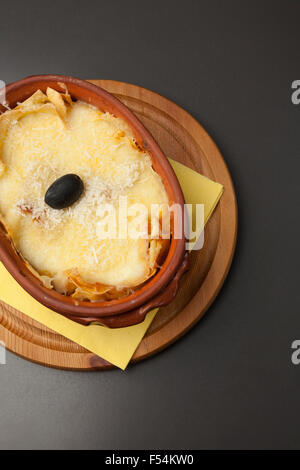 Portion Lasagne in einem Keramiktopf auf einem Holzsockel Stockfoto