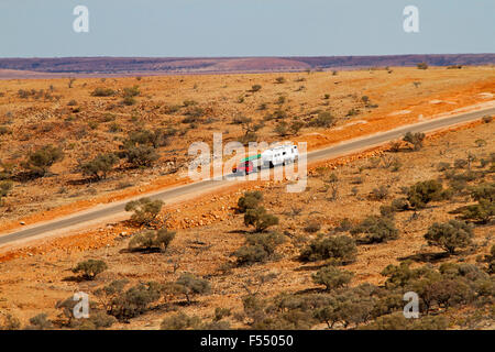 Roten Vierrad Antrieb Fahrzeug abschleppen Wohnwagen auf australische Outback Straße durch weite karge rote Landschaft unter blauem Himmel Stockfoto