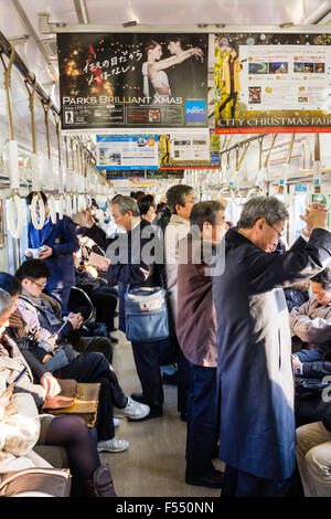 Japan, Osaka. Innen voll besetzt Nankai Bahn S-Bahn Wagen. Pendler sitzen und stehen. Winter also Leute Mäntel tragen. Stockfoto