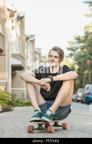 Nachdenklicher junger Mann sitzt auf Skateboard im freien Stockfoto