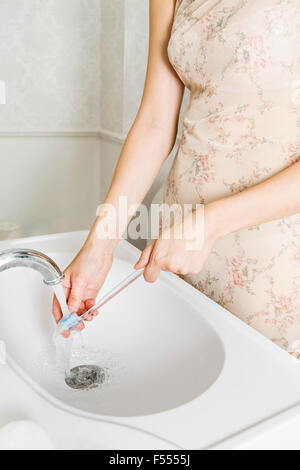 Mittelteil der Frau waschen Zahnbürste am Waschbecken im Bad Stockfoto