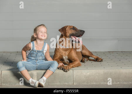 Glückliches Mädchen mit Hund auf Bürgersteig im Freien sitzen Stockfoto