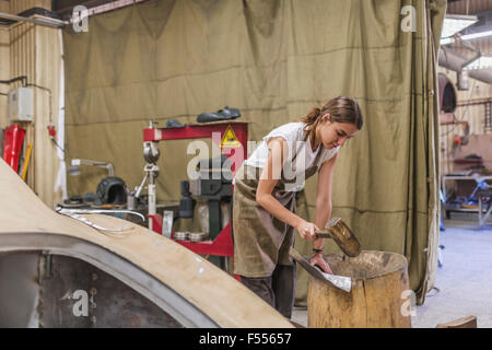 Weibliche Mechaniker trifft Metall auf Holzfass in garage Stockfoto