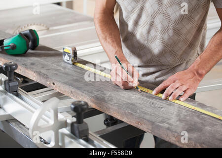 Mittelteil von männlichen Carpenter Messung Plank am Schiebetisch sah in Werkstatt Stockfoto