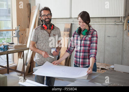 Männliche und weibliche Tischler mit Blaupause im Workshop lachen Stockfoto