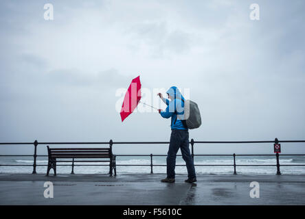 Mann mit rotem Regenschirm an windigen/stürmischen Tagen. VEREINIGTES KÖNIGREICH Stockfoto