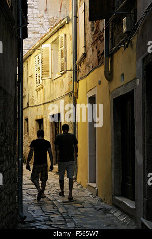 Zwei junge Männer, die zu Fuß in eine schmale gepflasterte Gasse in Rovinj, Istrien, Kroatien Stockfoto