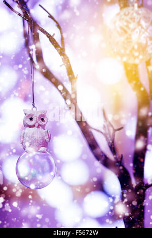 Festliche Weihnachten Hintergrund. Spielzeug Eule Vogel sitzt auf Glas Christbaumkugel unter gezeichneten Schneefall. Märchenhafte Postkarte. Festliche Stimmung. Stockfoto