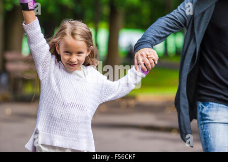 Kleine entzückende Mädchen Inline Skates im Park mit ihrem Vater Stockfoto