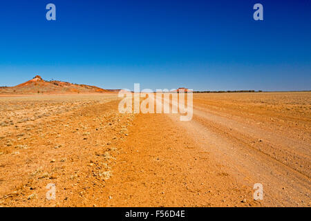 Lange Outback Feldweg über baumlose rote Prärie mit niedrigen Hügel am fernen Horizont unter blauem Himmel, western Australia, Queensland Australia Stockfoto