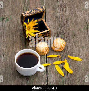 Tasse Kaffee, offenen Sarg mit einer Blume zwei Verknüpfung von Cookies und Blütenblätter, ein Still-Leben auf ein alter Tisch, ein Thema Lebensmittel und dr Stockfoto