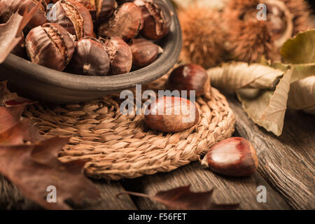 Gebratene Kastanien auf einem rustikalen Holztisch mit Herbst Blätter im Hintergrund. Stockfoto