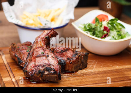 Gegrillte Lammkoteletts auf ein Schneidbrett aus Holz mit einer Portion Salat und Pommes frites Stockfoto