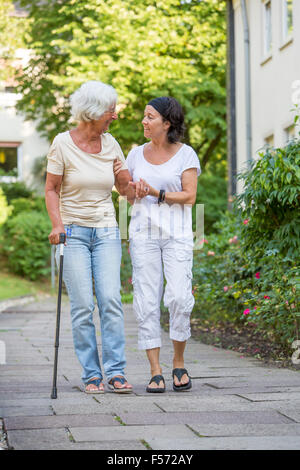 Altenpflege zu Hause, Krankenschwester kümmert sich um eine ältere Frau zu Fuß mit Gehhilfen, Stockfoto