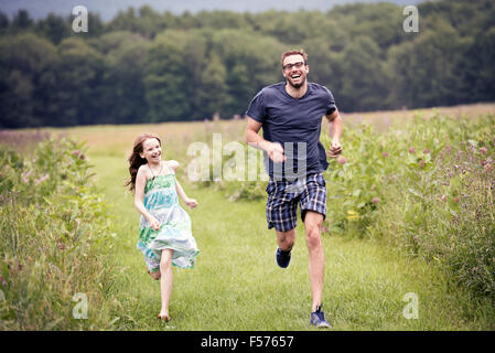 Ein Mann und ein junges Kind läuft durch eine Wildblumenwiese. Stockfoto