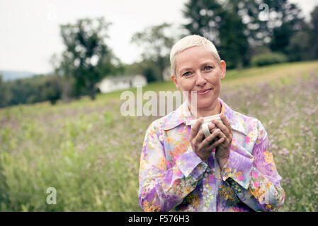 Eine Frau mit ihren Händen, um eine Kaffeetasse, sitzen auf einer Wiese gewickelt. Stockfoto