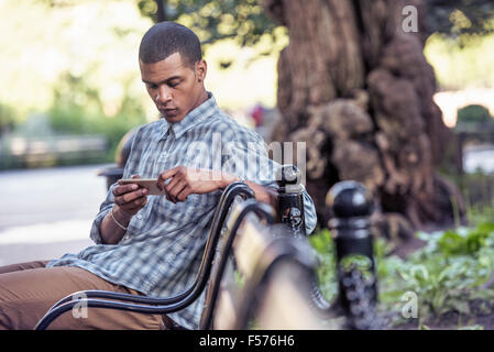 Ein Mann sitzt auf einer Parkbank mit seinem Smartphone Stockfoto