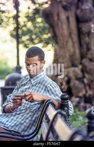 Ein Mann sitzt auf einer Parkbank mit seinem Smartphone Stockfoto