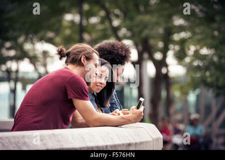 Ein Mann und zwei Frauen, die mit smart phones steht in einem park Stockfoto