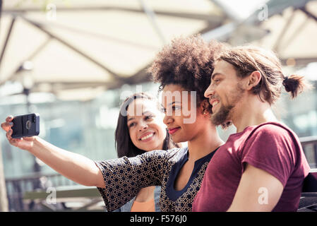 Drei Menschen, ein Mann und zwei Frauen, Einnahme von Selfies in einem Stadtpark Stockfoto