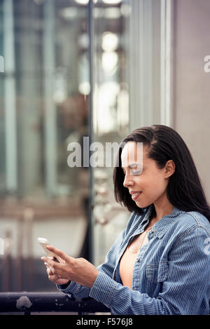 Eine junge Frau, die ihr Handy auf einer Stadtstraße überprüfen Stockfoto