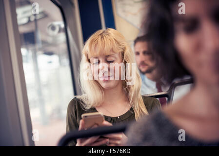 Eine blonde Frau in einem Bus, blickte auf ihr Handy Stockfoto