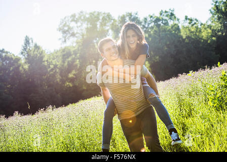 Ein paar, ein Mann einer jungen Frau ein Huckepack, ein Spaziergang durch eine Blumenwiese im Sommer. Stockfoto