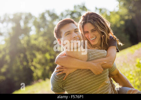 Ein paar, ein Mann einer jungen Frau ein Huckepack, ein Spaziergang durch eine Blumenwiese im Sommer. Stockfoto