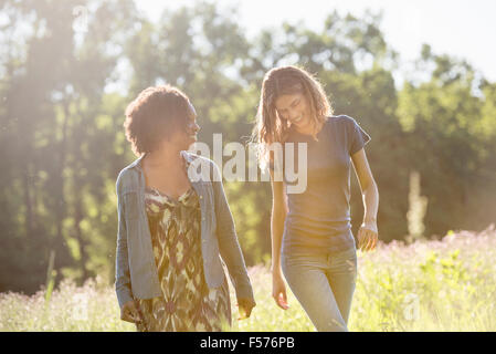 Zwei Frauen zu Fuß durch ein Feld reden und lachen. Stockfoto