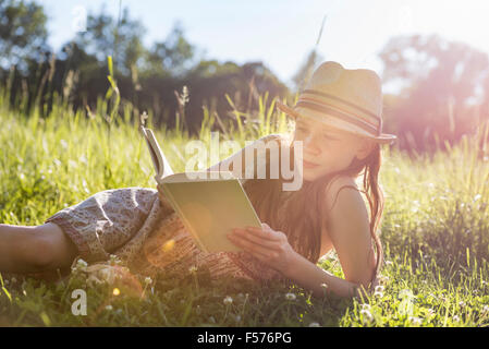 Ein junges Mädchen in einem Strohhut liegen auf dem Rasen, ein Buch zu lesen. Stockfoto