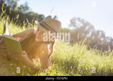 Ein junges Mädchen in einem Strohhut liegen auf dem Rasen, ein Buch zu lesen. Stockfoto