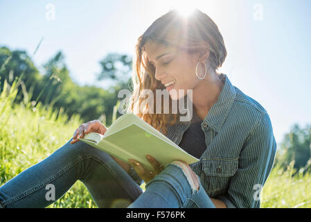 Eine junge Frau sitzt in der Sonne, ein Buch zu lesen Stockfoto