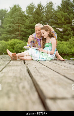 Ein kleines Kind mit einem offenen Buch auf dem Schoß neben einer reifen Frau zu lesen. Stockfoto