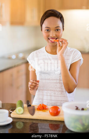 schöne Afrikanerin machen Salat in Küche und Tomaten schmecken Stockfoto