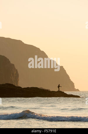 Perranporth Cornwall England.  Ein Mann Meeresangeln von den Felsen als Sonnenuntergang Ansätze mit großen Felsen im Hintergrund. Stockfoto