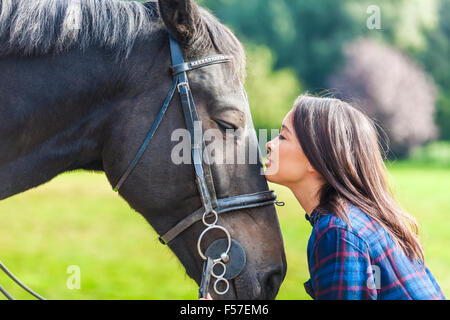 Schöne glückliche asiatischen eurasischen junge Frau oder Mädchen trägt karierte Karohemd, Lächeln und den Kopf auf ihrem Pferd in Sonne ruht Stockfoto