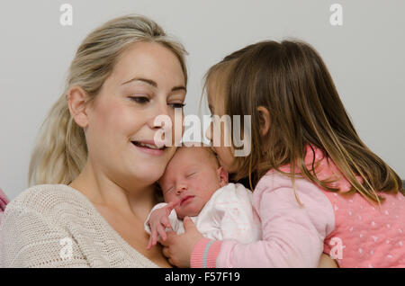 Mutter und einen Tag alt Mädchen von der Geburt im Krankenhaus zurück nach Hause. Drei Jahre alte Schwester ihre neue Schwester zu küssen. VEREINIGTES KÖNIGREICH. Stockfoto